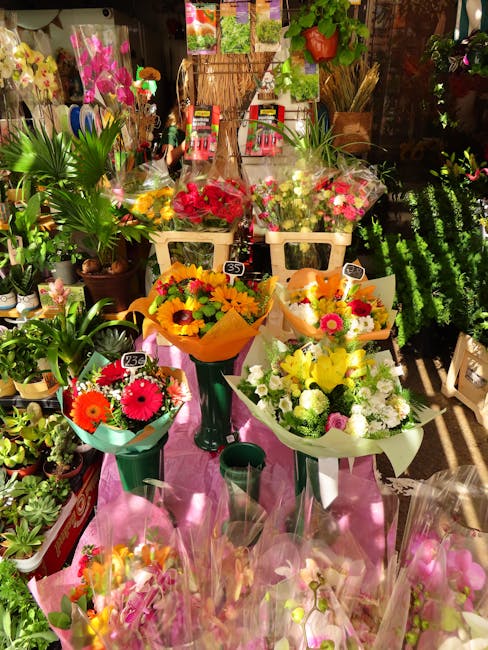 A vibrant florist display featuring a variety of fresh floral arrangements and bouquets. Central to the image are three bouquets wrapped in colorful paper, with the one in the middle primarily yellow-