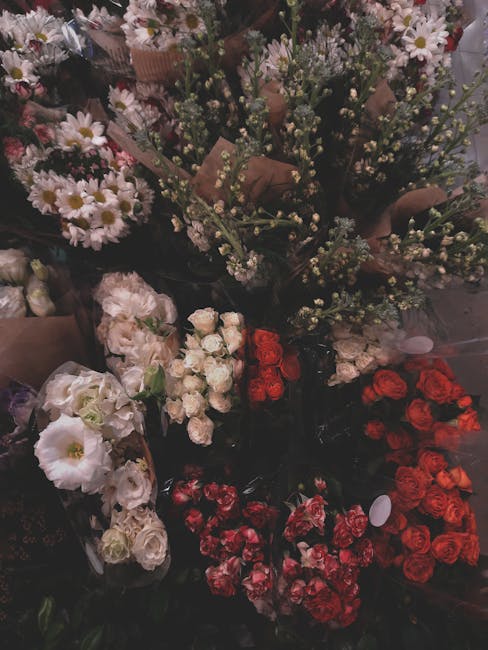 A variety of fresh floral arrangements displayed closely together. The image features clusters of small white daisy-like flowers with yellow centers, delicate light purple sprigs, and lush green folia