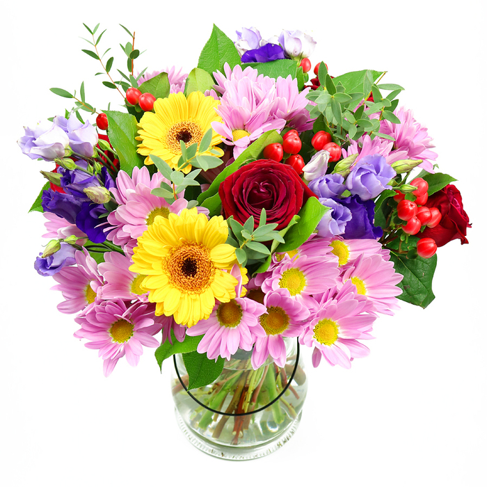 In a tall, cylindrical glass vase, a lush and colourful bouquet rises up like a joyful focal point for a Lewisham living room or office. At its heart are sumptuous deep red roses, each one unfolding in layers of velvety petals that give the arrangement emotional depth and a timeless romantic touch. Set alongside them, two golden yellow gerbera daisies face outward, their dark brown-orange centres and wide open petals evoking small suns, instantly lifting the mood of the design. Surrounding this strong centre, clusters of soft pink daisies or chrysanthemums spread in generous sprays, their fine petals and bright yellow centres creating an airy, approachable softness. Interlaced with these pinks are graceful stems of purple and lavender lisianthus; their slightly ruffled, bell-shaped blooms add coolness to the palette and an elegant vertical line, like accents of colour glimpsed among trees in nearby Manor House Gardens. Dotted between the flowers, rounded, glossy red hypericum berries provide an extra layer of visual interest, introducing distinct spheres of colour and texture that invite a closer look. A rich mix of greenery frames the bouquet, from broad, deep green leaves that anchor the form to slender, lighter green shoots and sprays that offer height and movement. The stems are clearly visible through the transparent vase, neatly gathered and immersed in fresh water, reflecting the confident hand of a professional florist familiar with Lewisham's tastes. Set against a crisp white backdrop, every hue, shape, and shadow becomes more defined, giving the bouquet a modern yet heartfelt feel, perfect for celebrations, thank-yous, or simply sending a warm thinking of you across Lewisham.